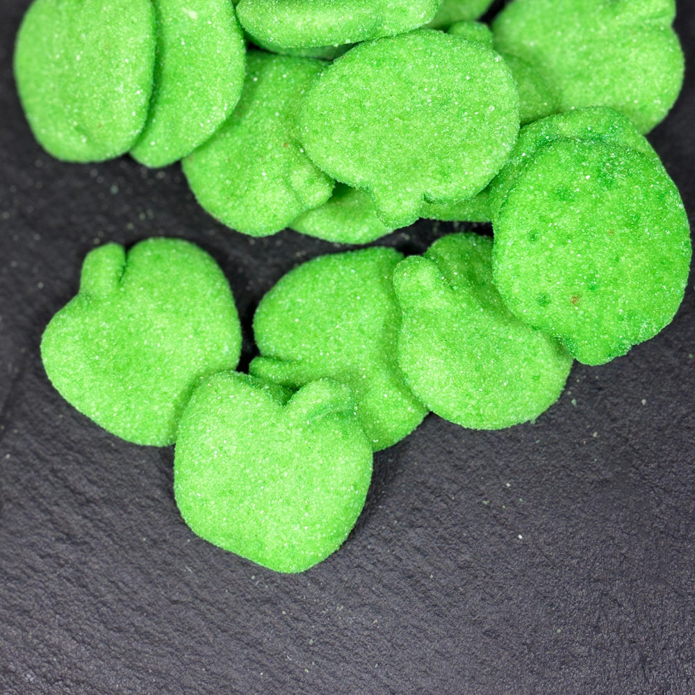 Bright green, sugar-coated, foam gummies shaped like apples, piled on a dark slate background.