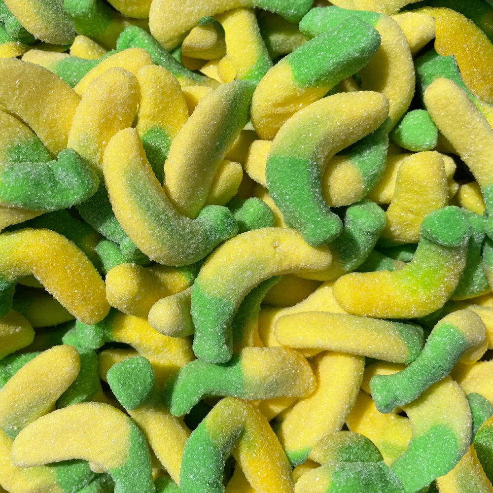 A close-up pile of sugar-coated gummy candies shaped like small curved bananas, with a bright yellow body and a green cap.