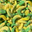 A close-up pile of sugar-coated gummy candies shaped like small curved bananas, with a bright yellow body and a green cap.