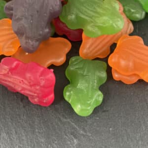 green, orange, red and purple jelly frogs on a dark stone background