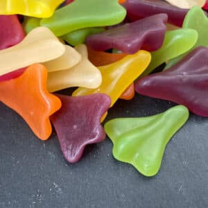 pile of green, oragne, yellow, beige and plum coloured jet plane gummies on a dark grey background