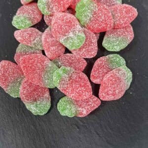 green and red coloured Fizzy Strawberry gummy lollies with a sugar coating, on a grey stone background
